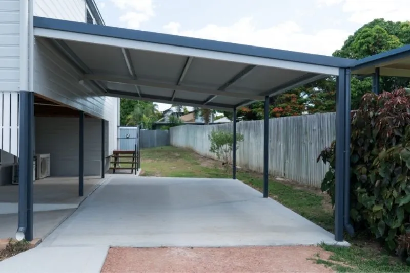Open steel-framed carport attached to a home beside a timber fence