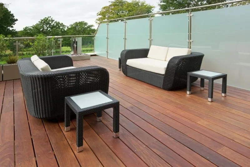 Timber deck with woven outdoor sofas and a glass balustrade overlooking a garden view