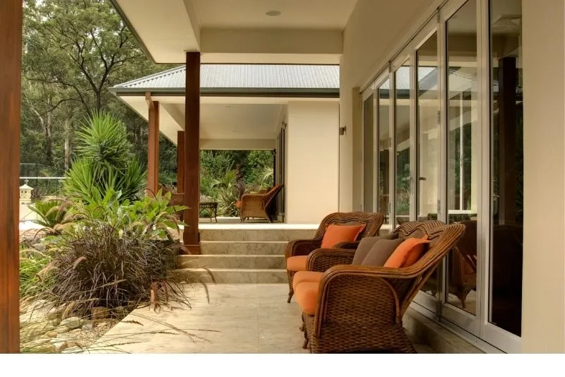 Timber-post verandah with wicker outdoor lounge chairs opening onto a home's interior