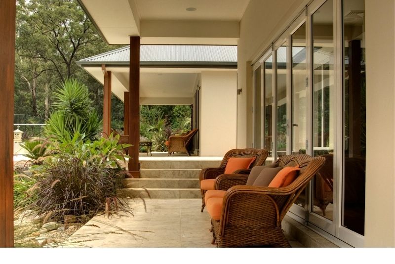 Timber-post verandah with wicker outdoor lounge chairs opening onto a home's interior